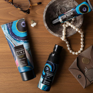 Cosmetic products including a tube of hand cream, spray bottle, and lip balm with decorative aboriginal packaging on a table