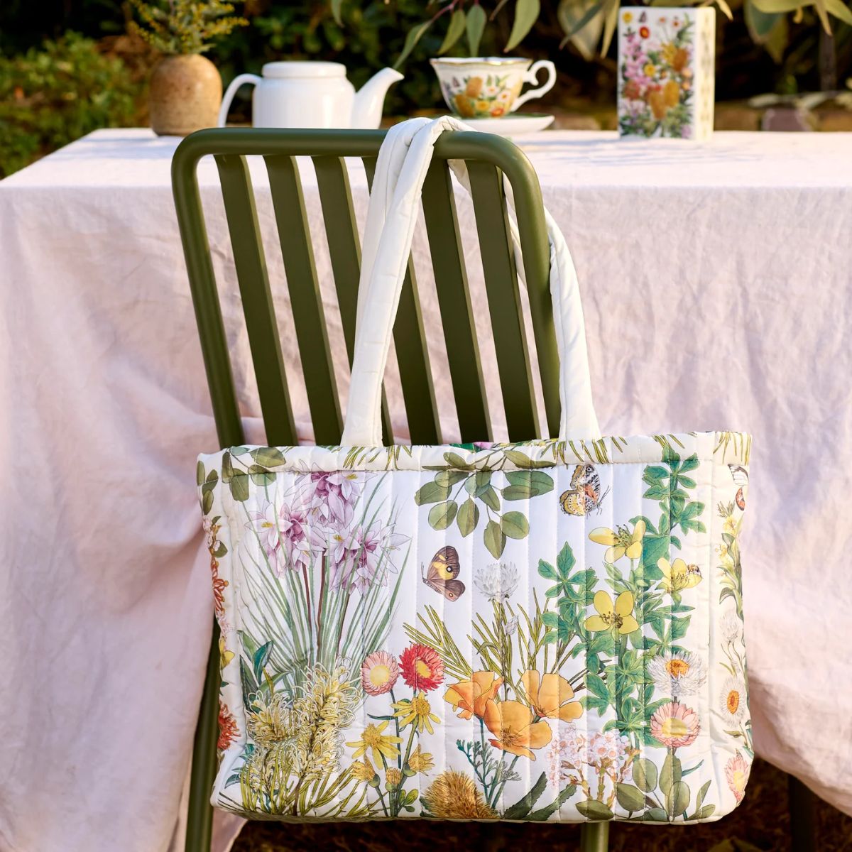 Floral-patterned tote bag on a chair with a table and teacups in the background