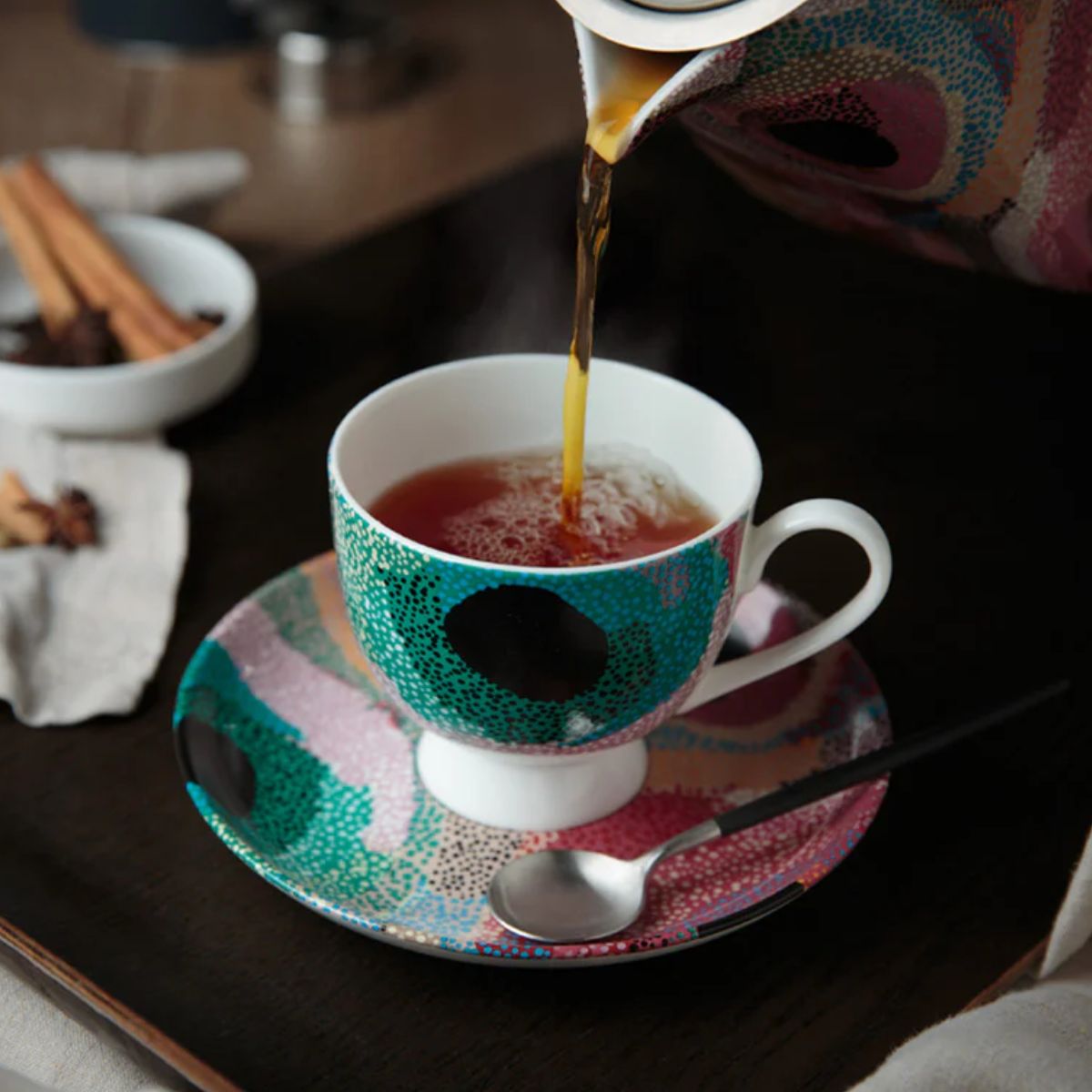 Tea being poured into a aboriginal teacup on a saucer with a spoon.