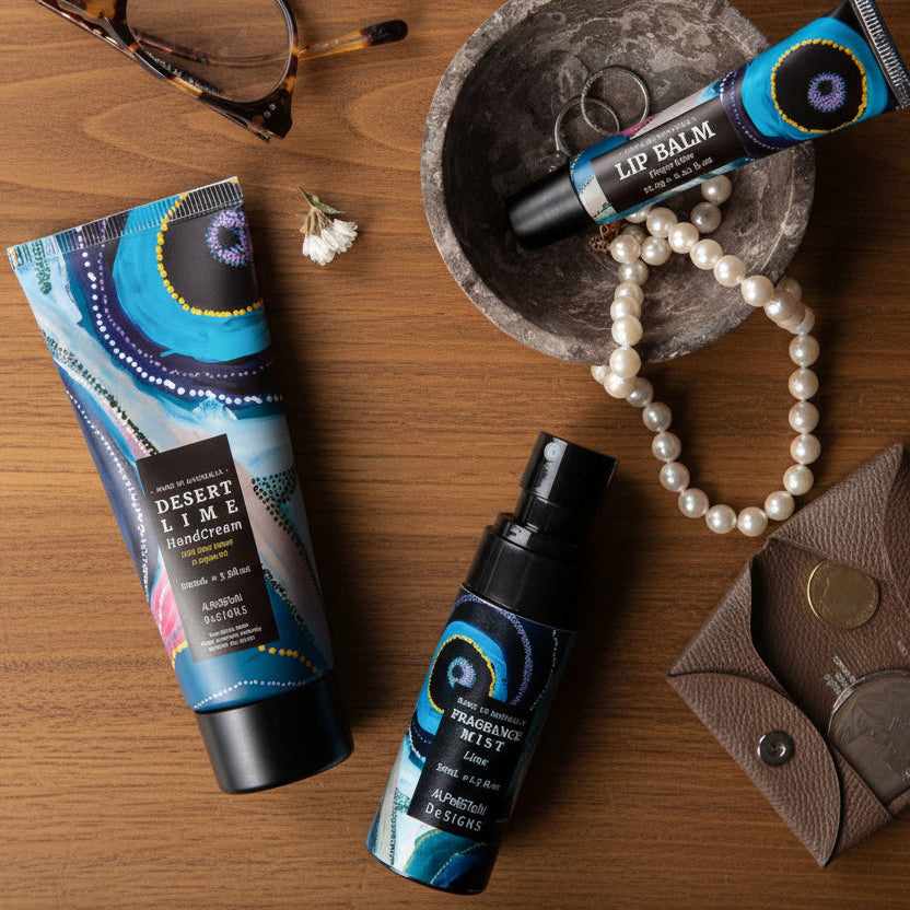 Cosmetic products including a tube of hand cream, spray bottle, and lip balm with decorative aboriginal packaging on a table